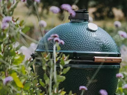 The Big Green Egg surrounded by flowers and greenery.
