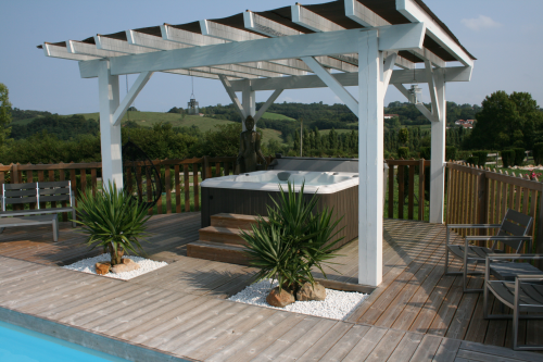 Outdoor hot tub installed on a patio underneath a pergola on a bright, sunny day.